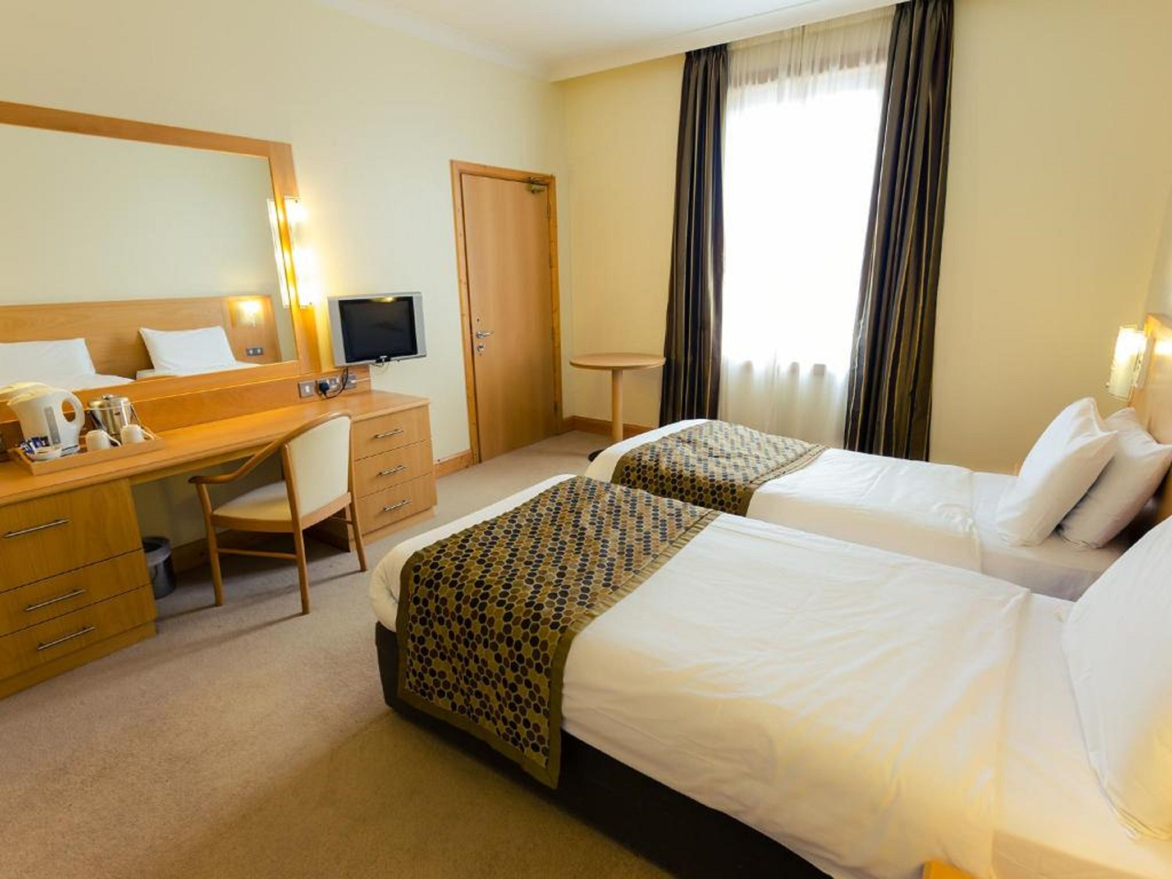 A hotel room with two beds, a desk, a chair, a television, and a window with curtains.