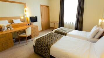 Een hotelkamer met twee bedden, een bureau, een stoel, een televisie en een raam met gordijnen.