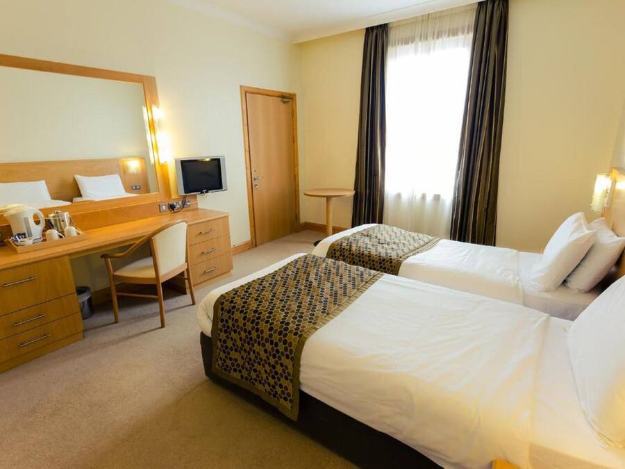A hotel room with two beds, a desk, a chair, a television, and a window with curtains.