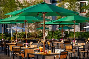 Mesas de comedor al aire libre con sombrillas verdes, sillas de madera y diversas bebidas.