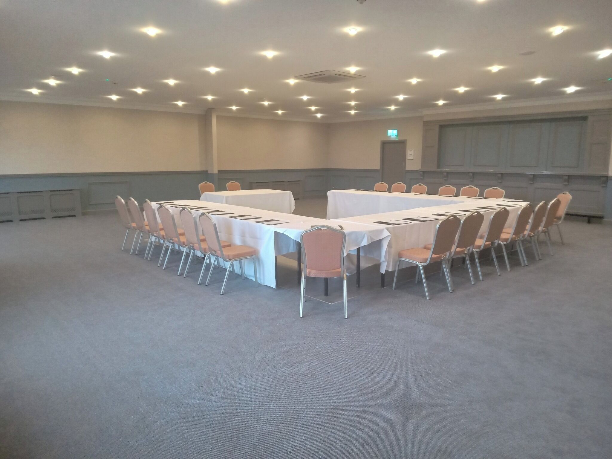 A conference room with round tables and chairs, carpeted floor, and recessed ceiling lights.