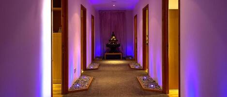 A hallway with a purple-lit pathway, wooden doors, and a small altar at the end.
