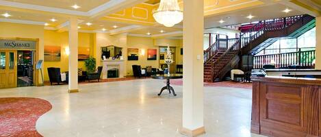 A spacious lobby with a grand chandelier, a staircase, and a reception desk.