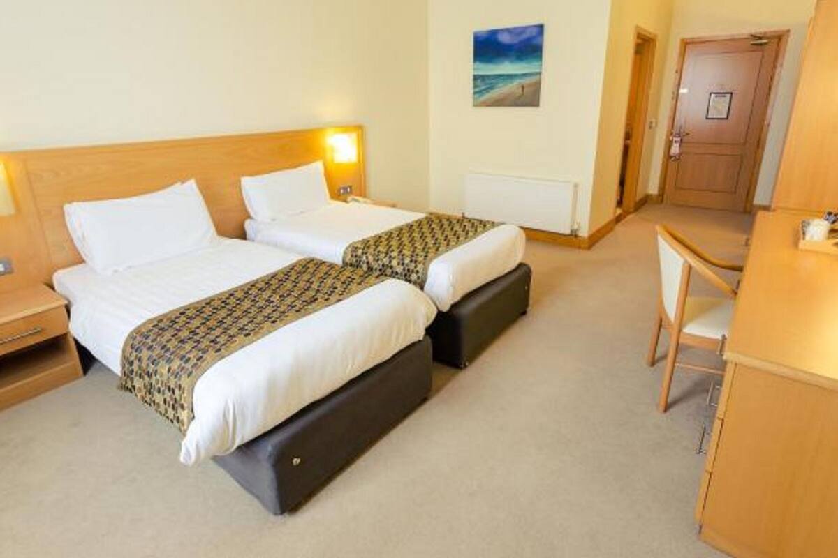 Een hotelkamer met twee bedden, een bureau, een stoel, een schilderij aan de muur en een deur.