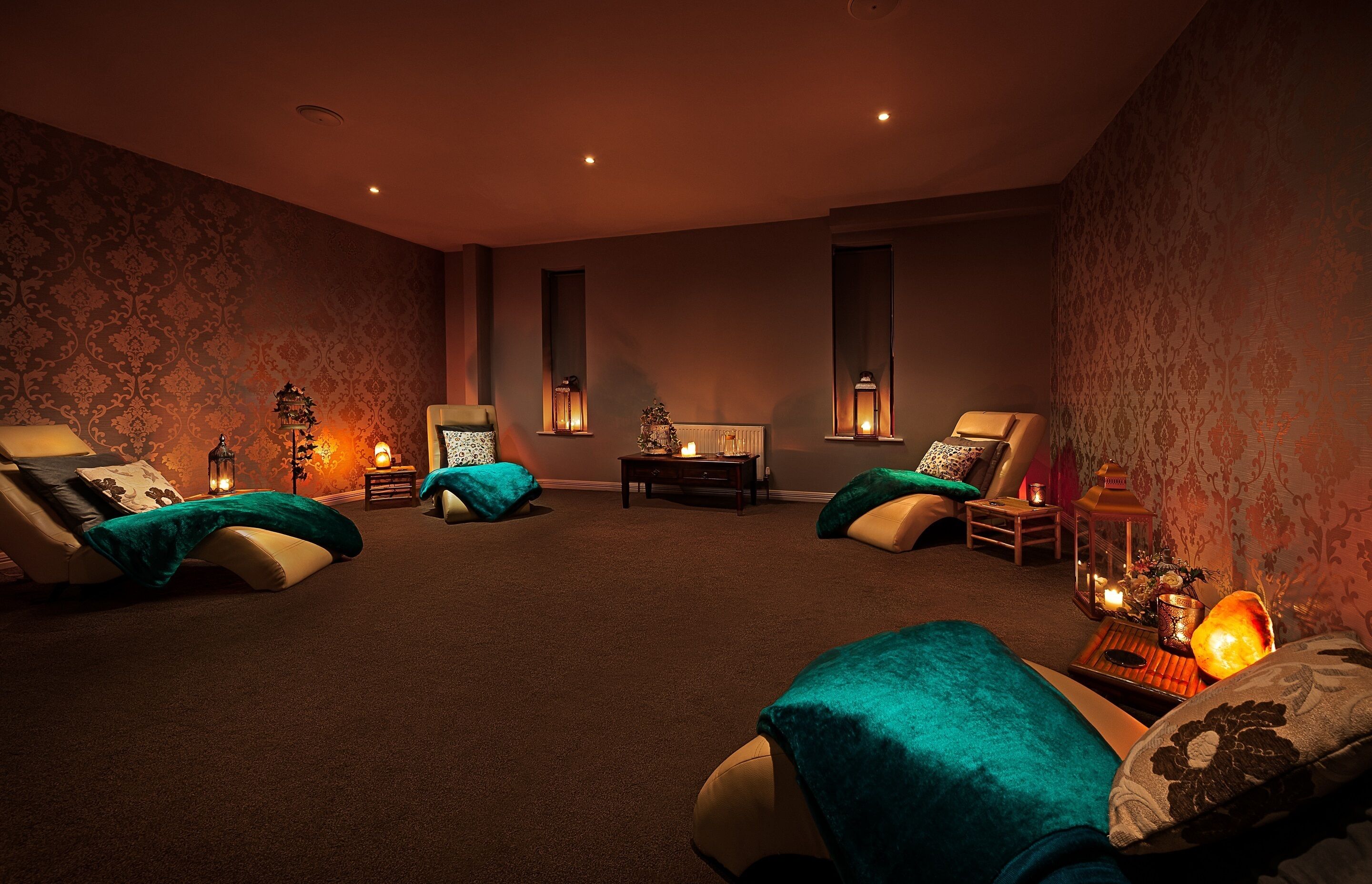 A room with four reclining chairs, a small table, and wall-mounted lamps.