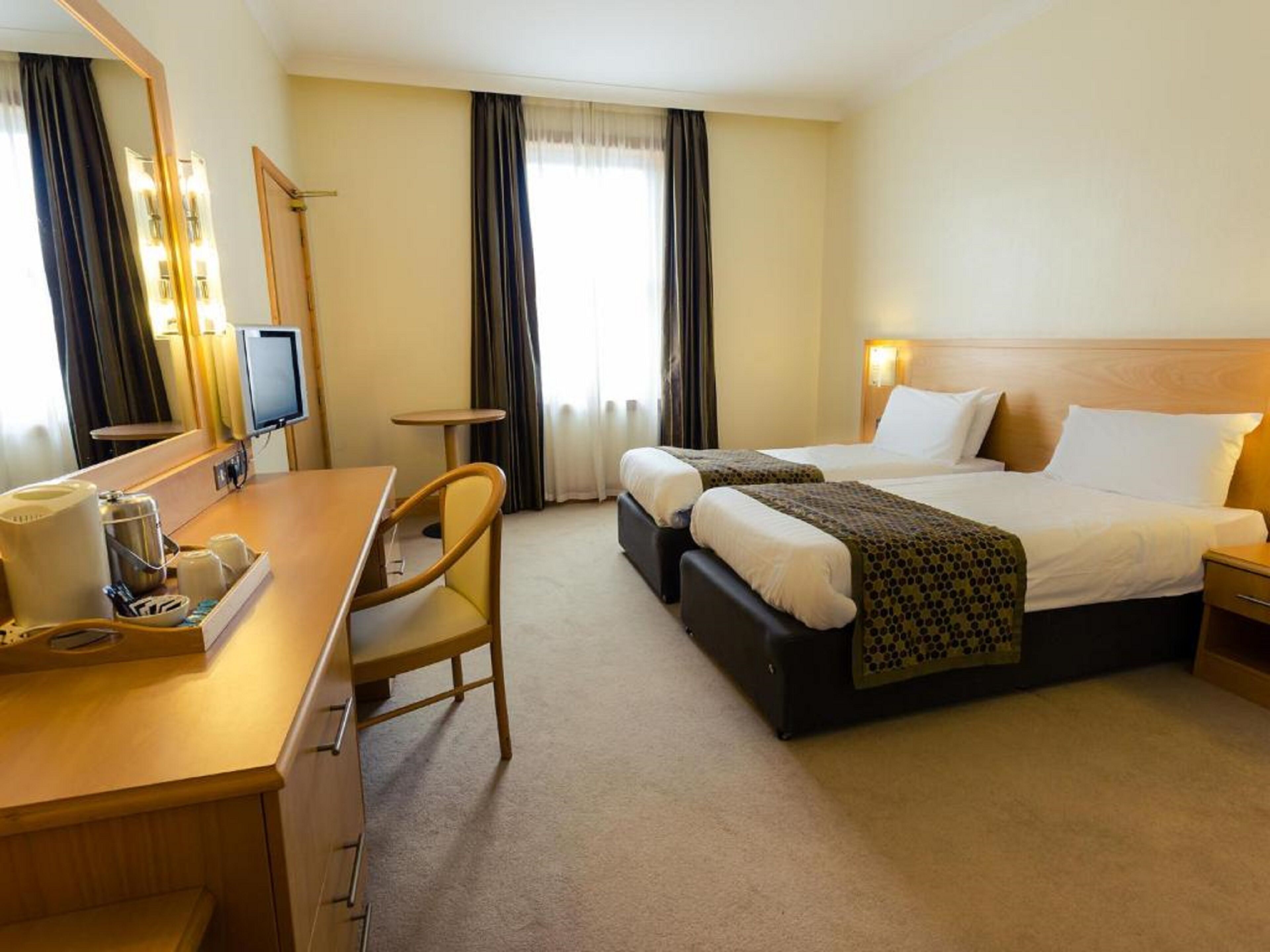 A hotel room with a bed, a desk, a chair, a television, and a window with curtains.
