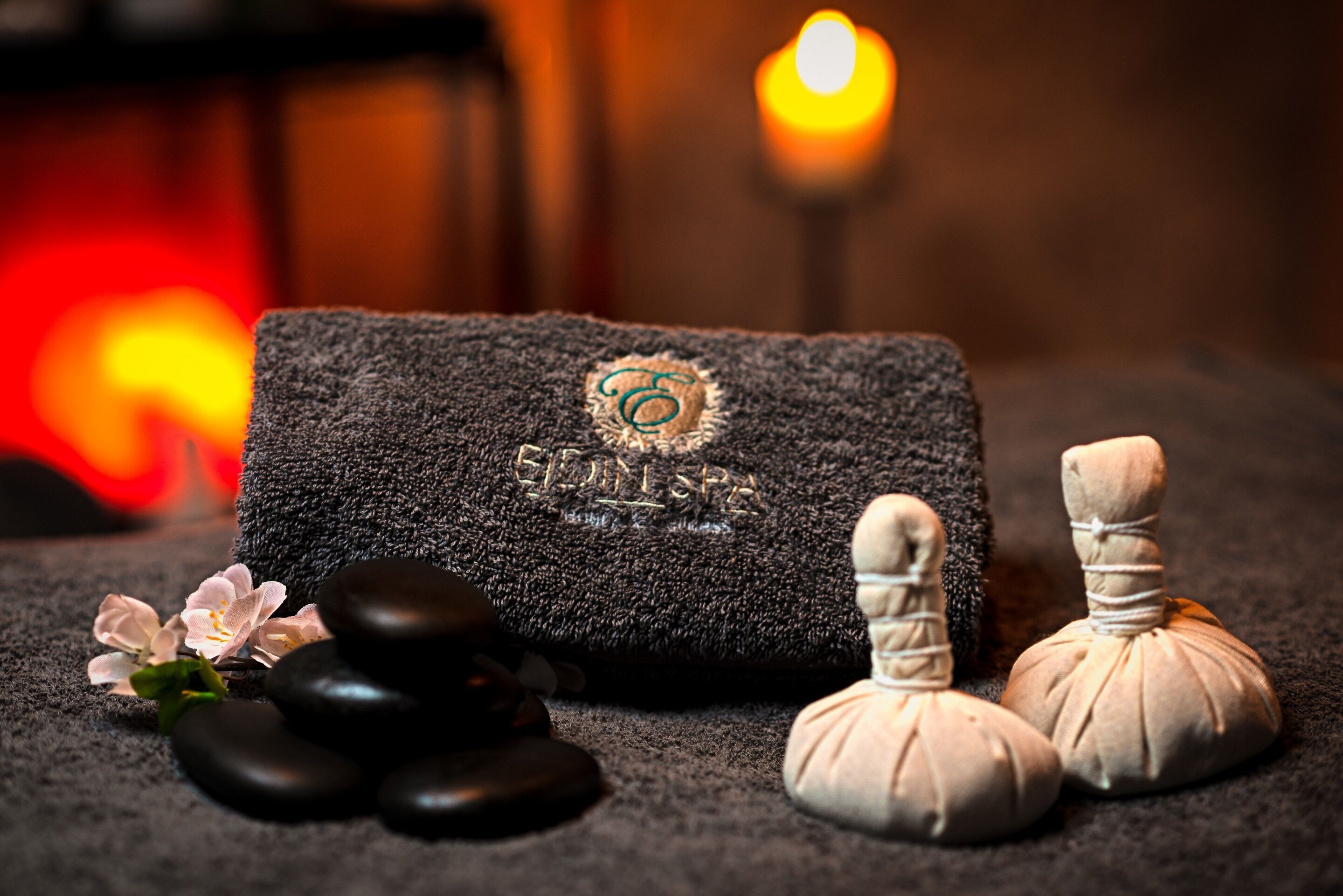 Un entorno de spa con una toalla, piedras de masaje y una vela.