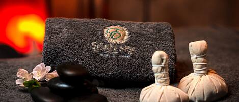 Un entorno de spa con una toalla, piedras de masaje y una vela.