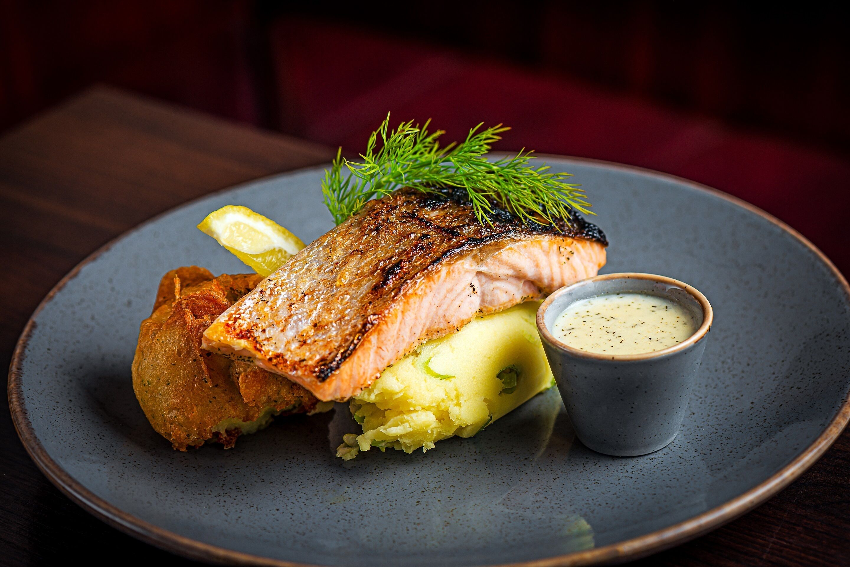 A plate with grilled salmon, mashed potatoes, and a small cup of sauce.