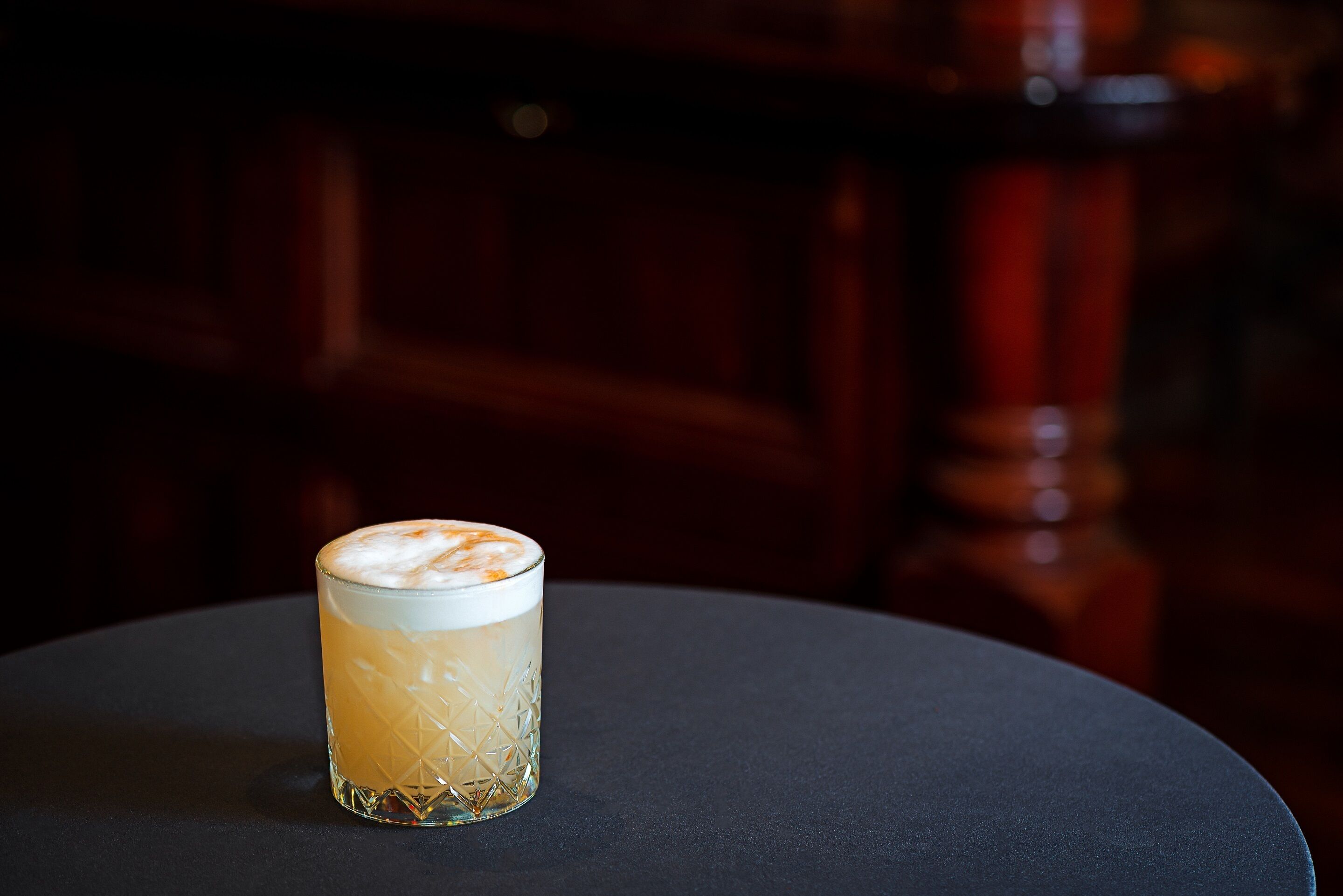 Un vaso de una bebida clara con espuma, sobre una mesa redonda de superficie oscura.