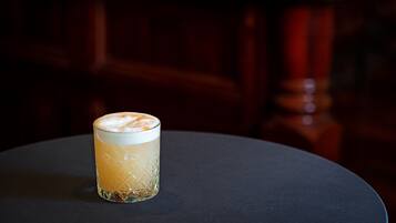 Un vaso de una bebida clara con espuma, sobre una mesa redonda de superficie oscura.