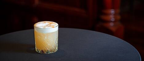 Un vaso de una bebida clara con espuma, sobre una mesa redonda de superficie oscura.
