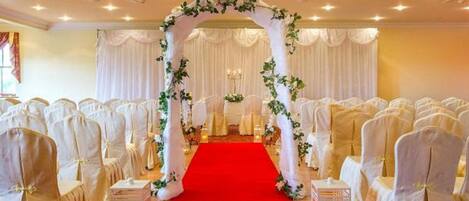Un pasillo de bodas con sillas blancas y una alfombra roja, que conduce a un arco decorado.