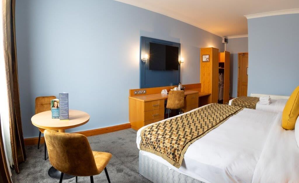 A hotel room with a bed, a desk, a chair, a round table, a wardrobe, and a television.