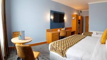 A hotel room with a bed, a desk, a chair, a round table, a wardrobe, and a television.
