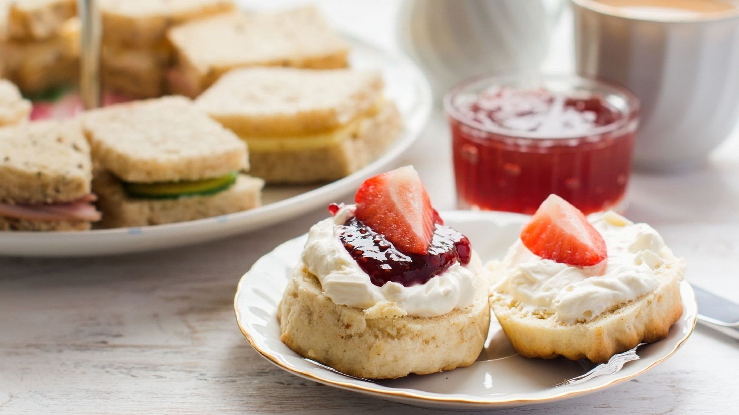 Un plato de scones con crema y fresas, un tarro de mermelada y una taza de té sobre una mesa.