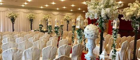 Un salón de banquetes con filas de sillas blancas, arreglos florales blancos y faroles blancos.