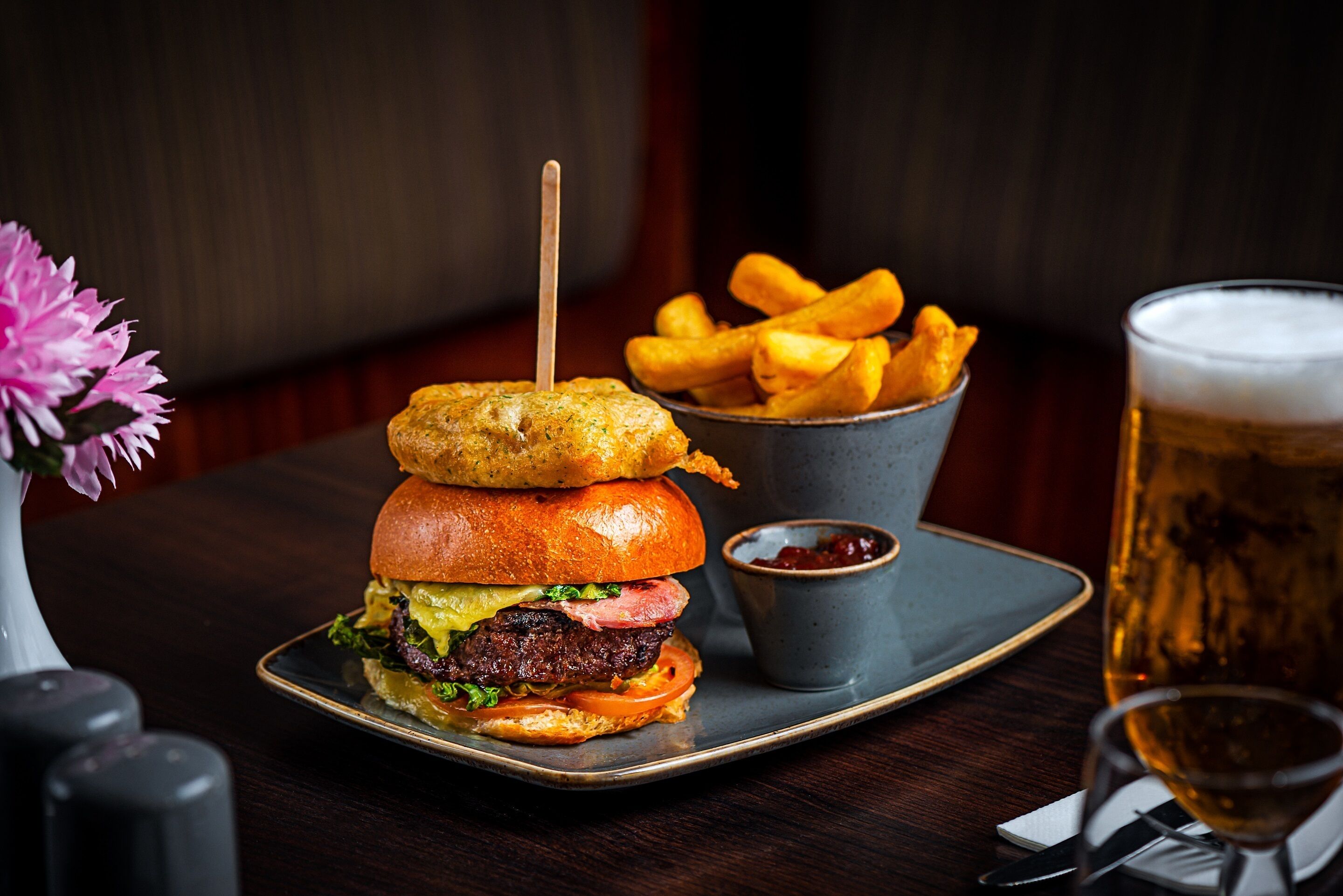 A burger with a side of fries and a glass of beer on a table.
