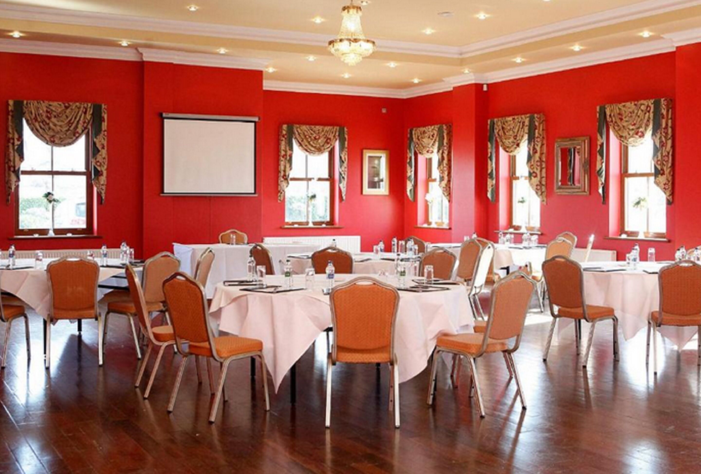 Une salle de conférence aux murs rouges, aux tables blanches et aux chaises orange.