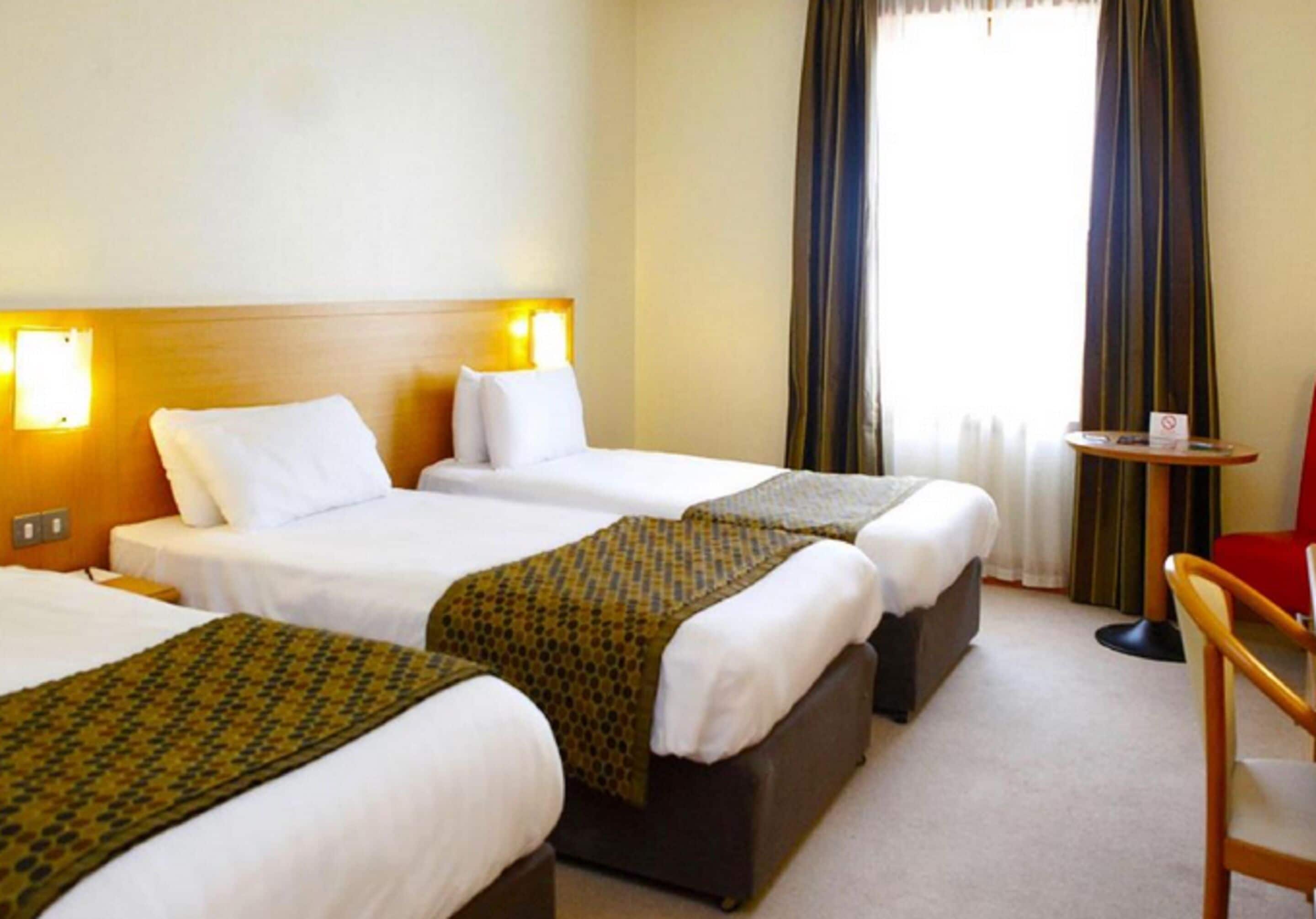 Ein Hotelzimmer mit drei Einzelbetten, einem kleinen Tisch und einem Stuhl.