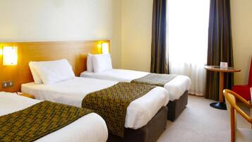 A hotel room with three single beds, a small table, and a chair.