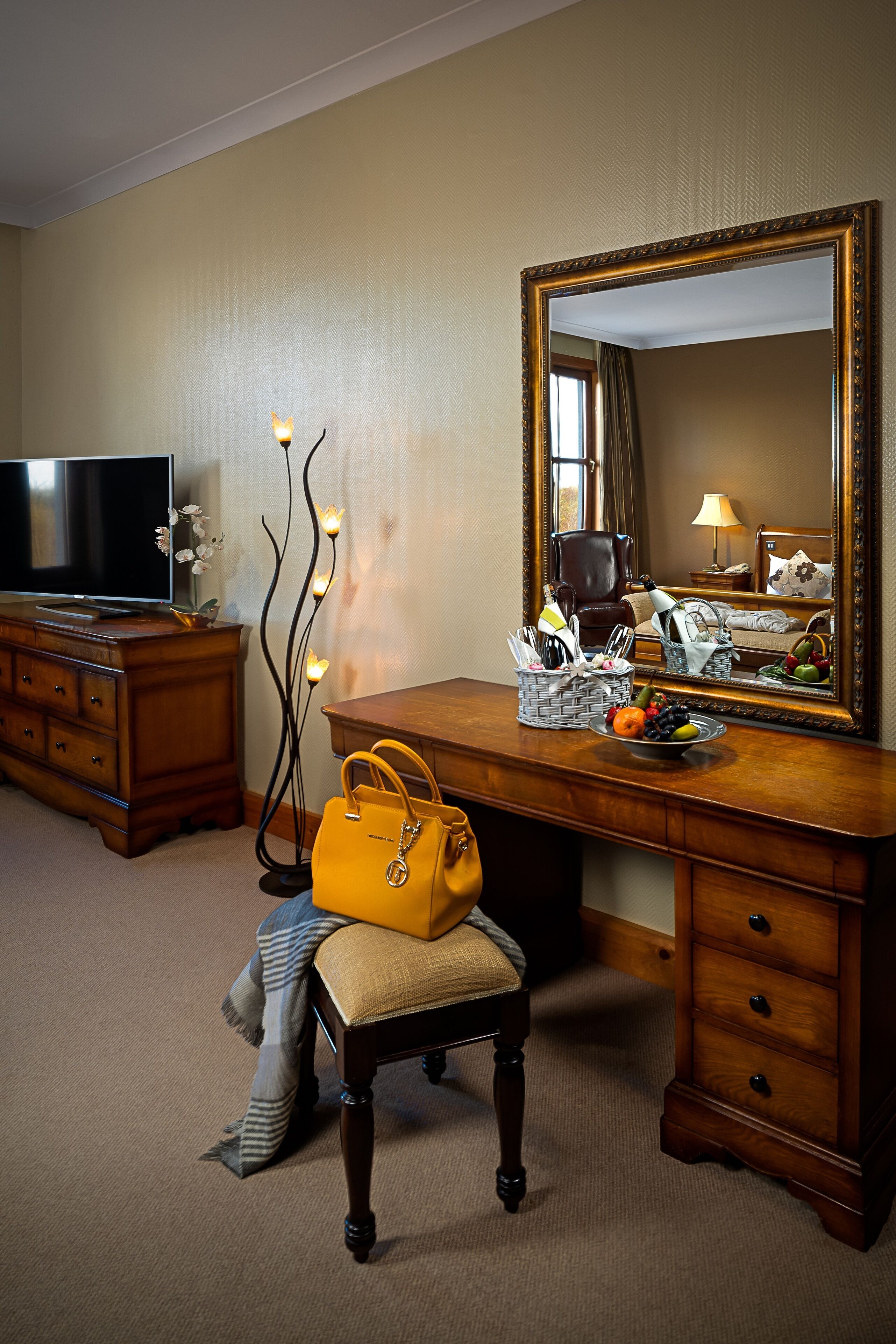 Une chambre d’hôtel avec un bureau en bois, une télévision, un miroir et un banc.
