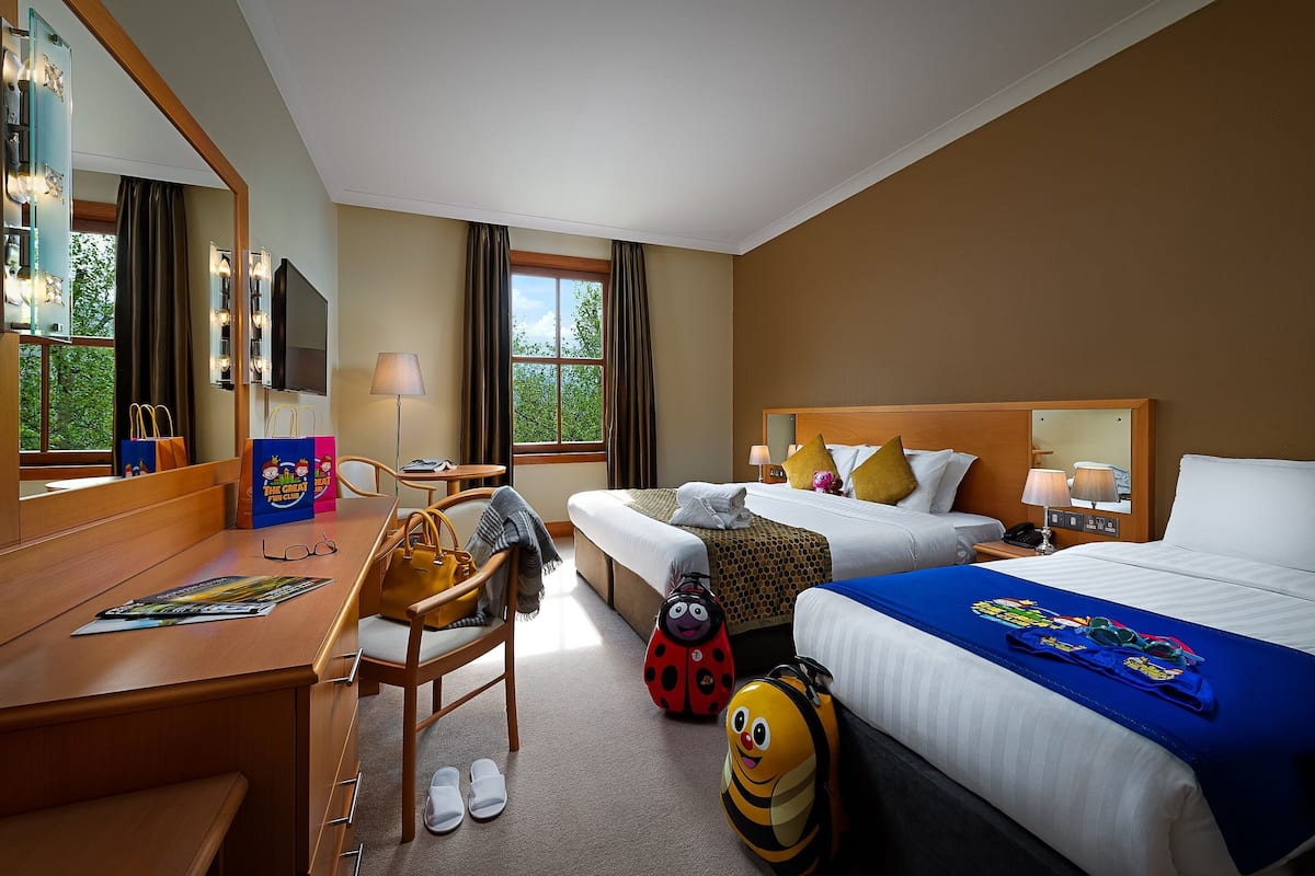 Een hotelkamer met een bureau, twee bedden, een spiegel en een raam met gordijnen.