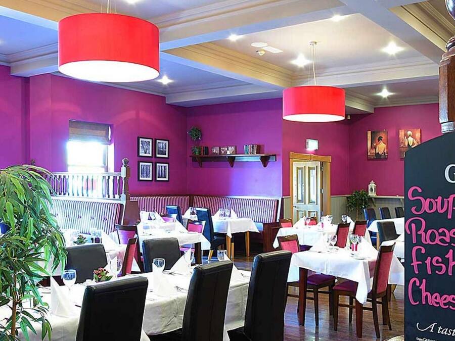 Un ristorante con pareti viola, luci a sospensione rosse e una lavagna con il menù che offre zuppa, arrosto, pesce e cheesecake.