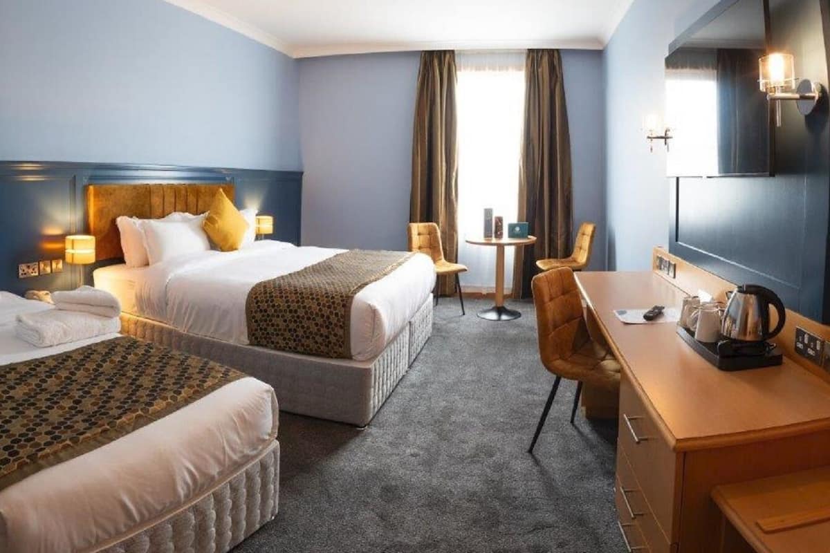 Een hotelkamer met twee bedden, een bureau, een stoel, een klein tafeltje en een televisie.