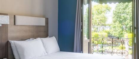 Habitación de hotel con dos camas, una mesita de noche con teléfono y vistas a un balcón con vegetación.