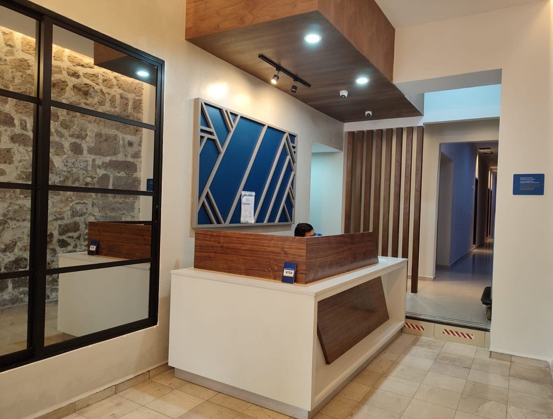 A reception desk with a mirror, a blue geometric wall decoration, and a wooden counter.