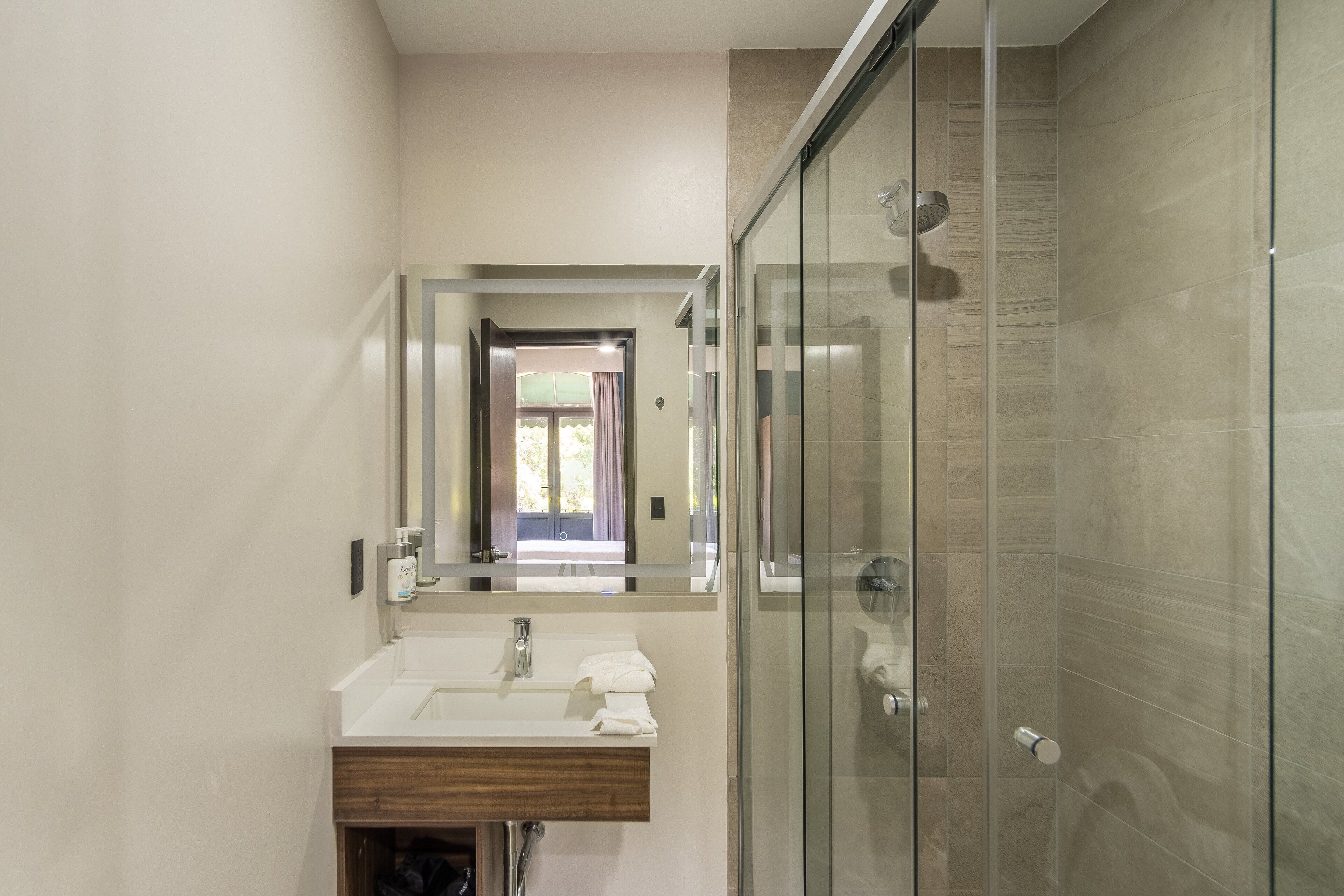 Un baño moderno con cabina de ducha de vidrio, un lavabo con tocador de madera y un espejo sobre el lavabo.