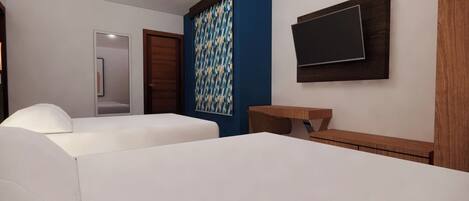 Habitación de hotel con cama, escritorio, televisor en la pared y cortina estampada.