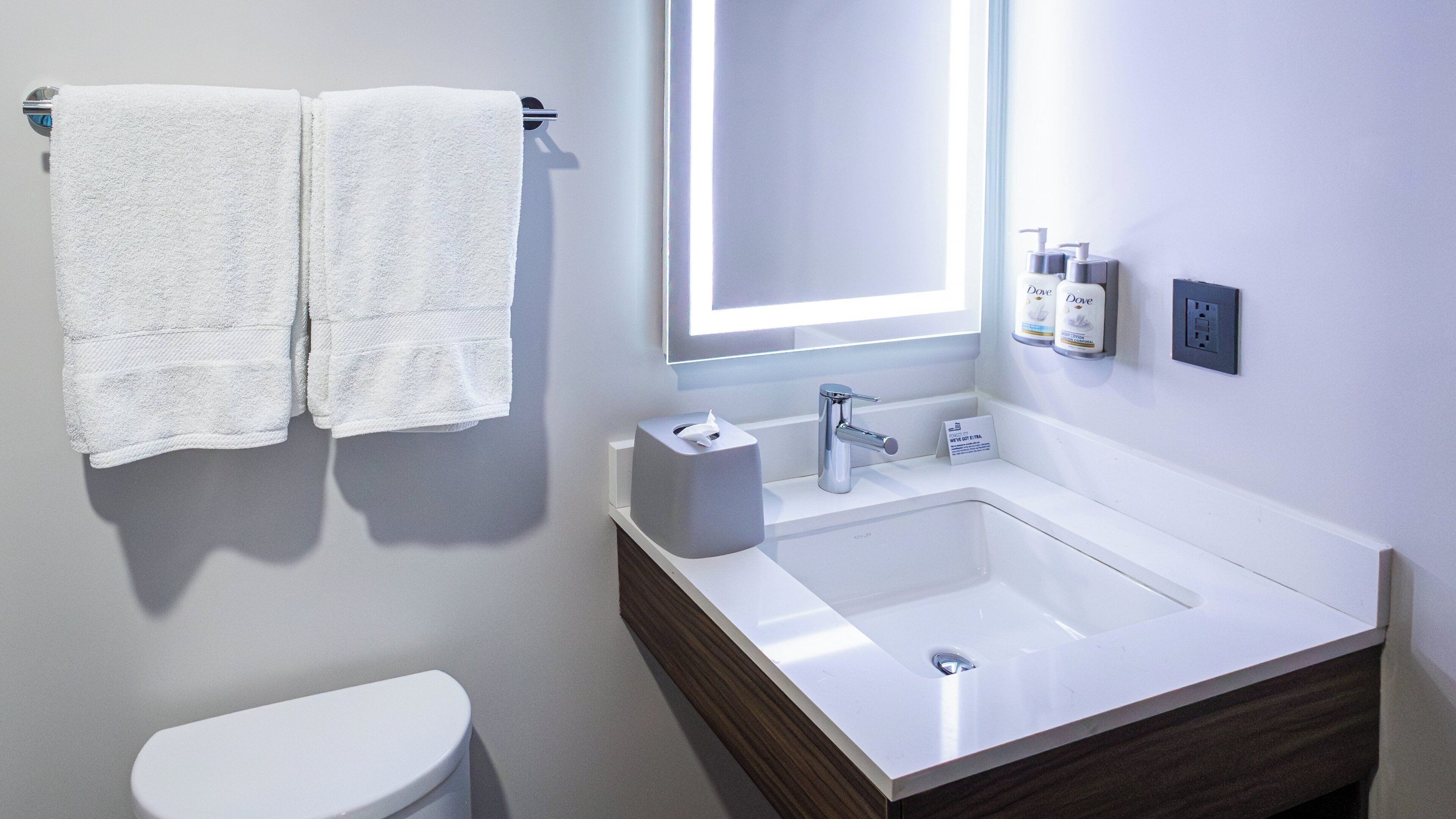 Een moderne badkamer met een wit wastafel, een spiegel, twee handdoeken, een toilet en toiletartikelen aan de muur.