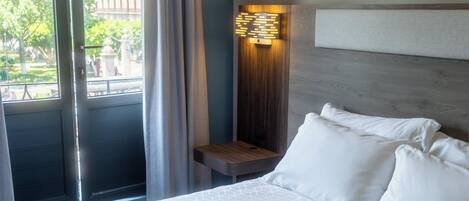 A hotel room with a bed, a nightstand, a wall-mounted light, and a window with curtains.