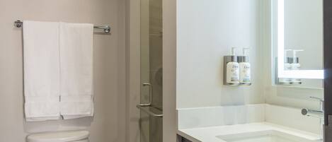 A modern bathroom with a toilet, a shower, and a vanity with a mirror.
