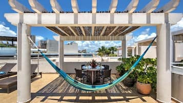 A rooftop patio with a pergola, a hammock, a dining table with chairs, and potted plants.