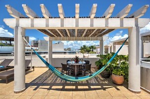 A rooftop patio with a pergola, a hammock, a dining table with chairs, and potted plants.