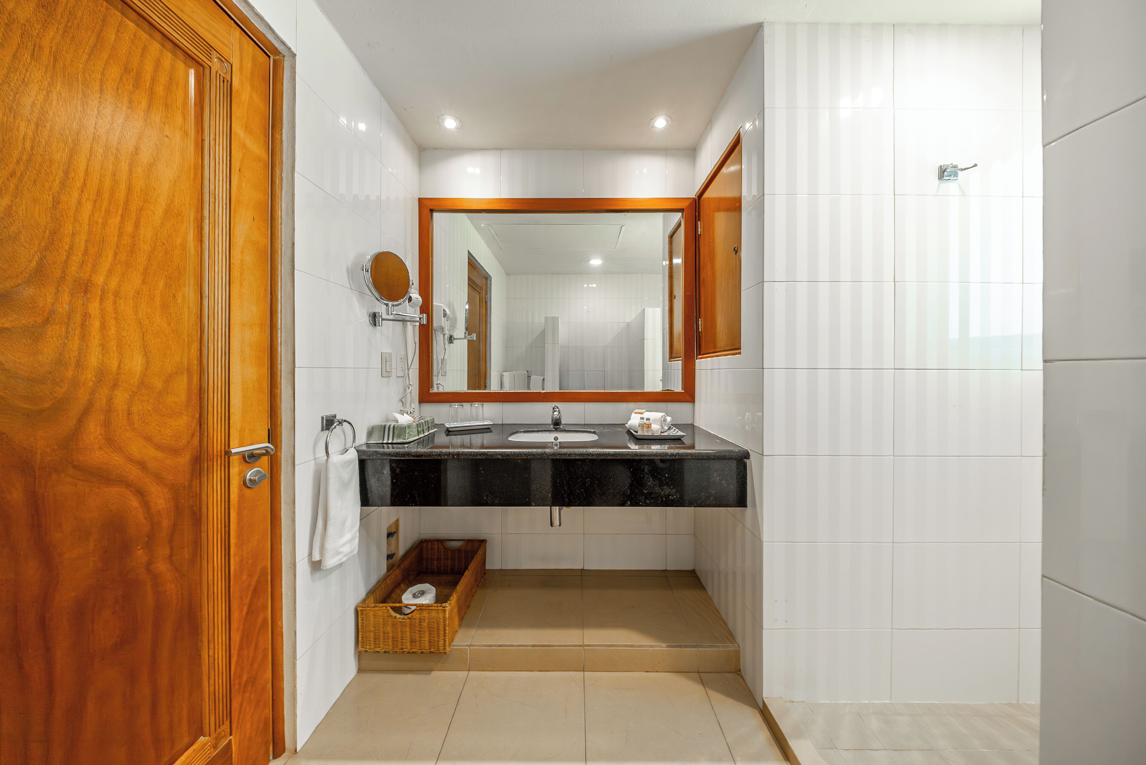 A bathroom with a wooden door, a black countertop sink, a mirror, and a tiled wall.