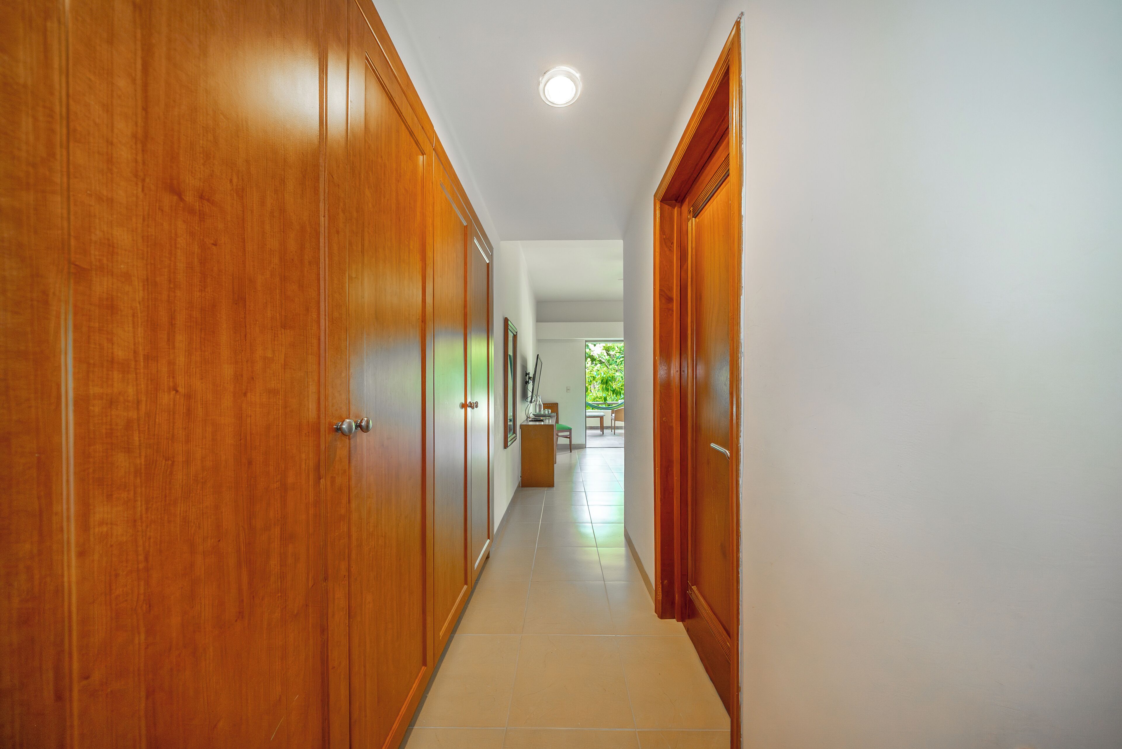 Um corredor com portas de madeira, chão de azulejos e vista para um quarto com mesa e cadeiras.