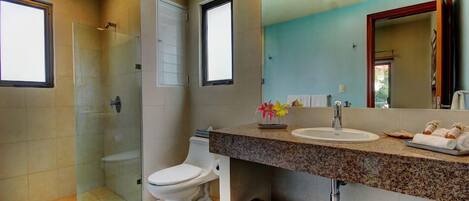Une salle de bain moderne avec une douche à parois de verre, des toilettes blanches, un lavabo avec un miroir et des paniers en osier.