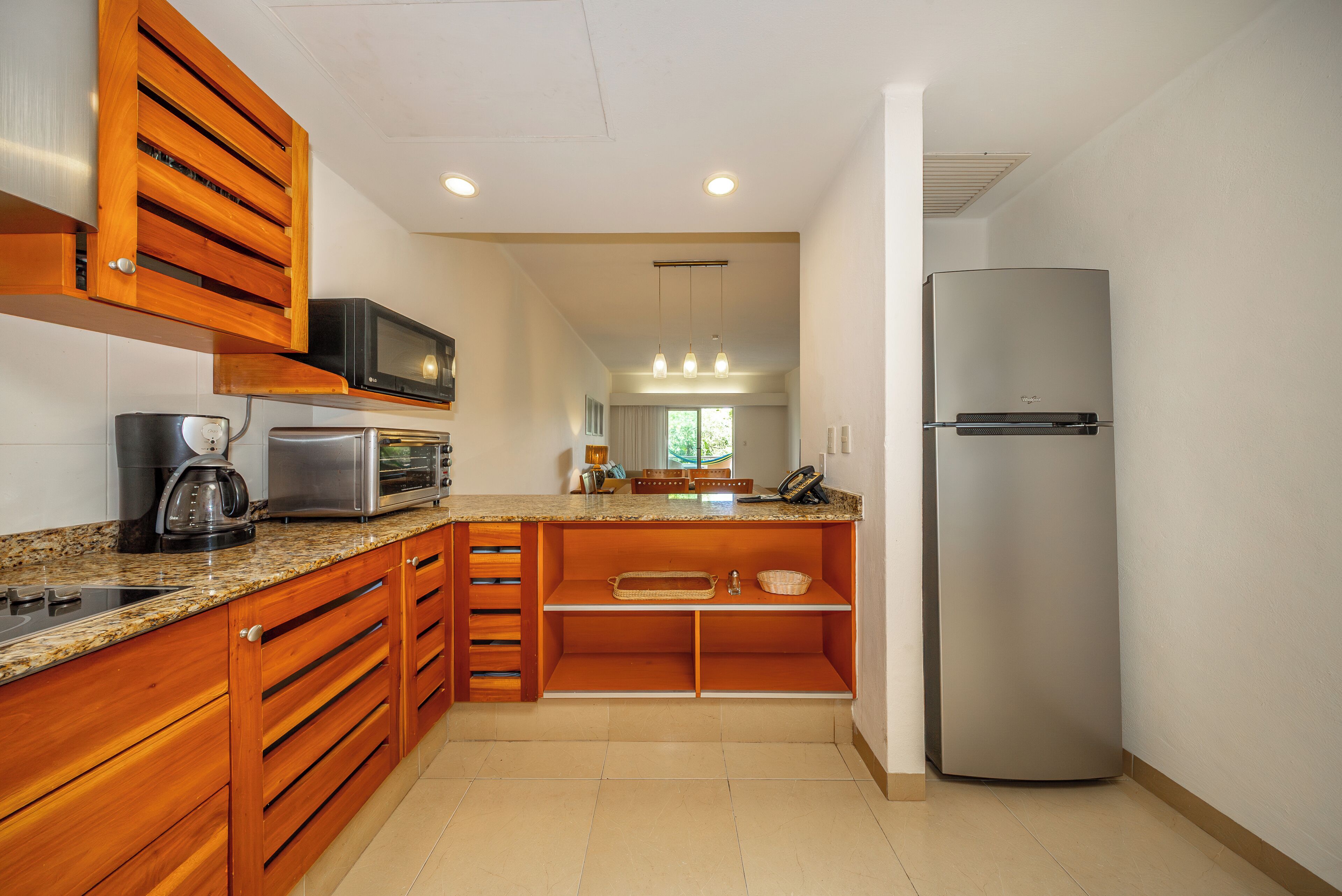 A kitchen with wooden cabinets, a stainless steel refrigerator, a microwave, and a granite countertop.
