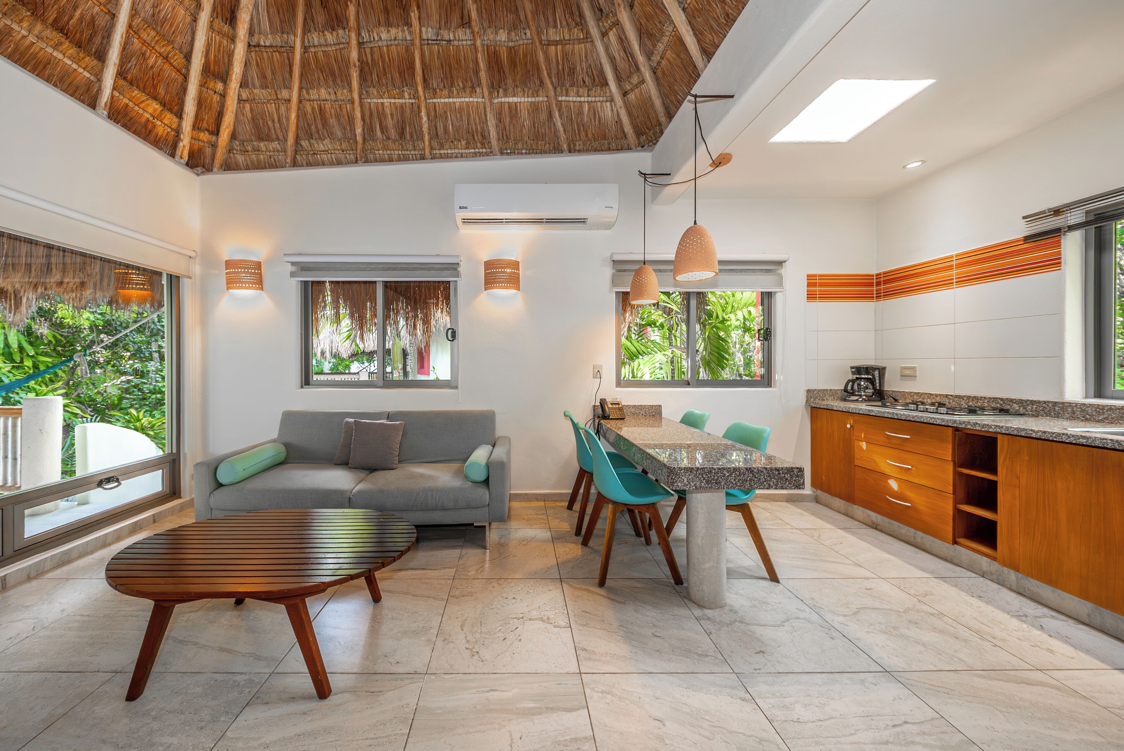 Ein modernes Interieur mit Essbereich, Küche und Wohnbereich, mit einem reetgedeckten Dach, großen Fenstern und Blick ins Grüne.