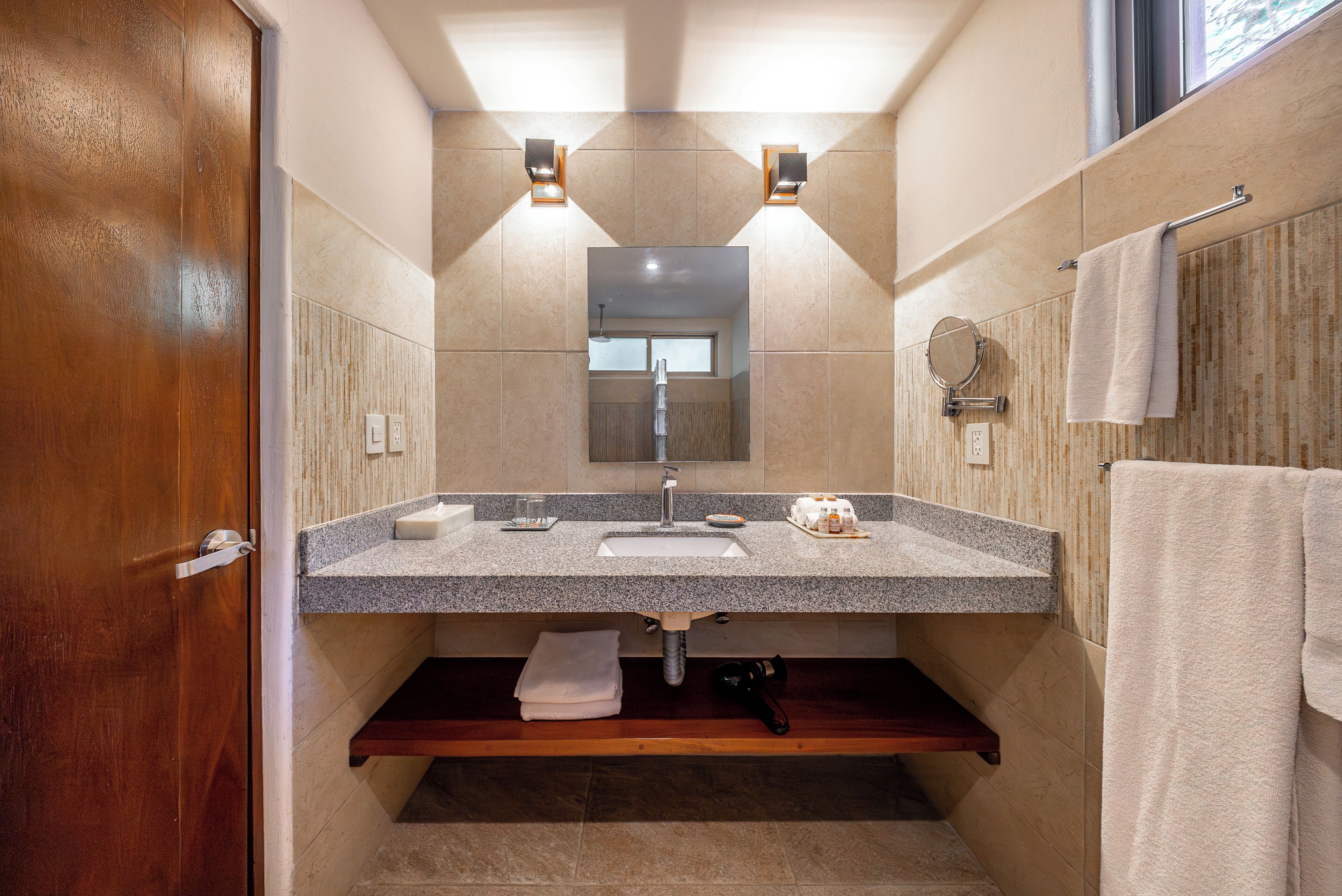 Un baño con puerta de madera, lavamanos con encimera de granito, toallero y espejo.