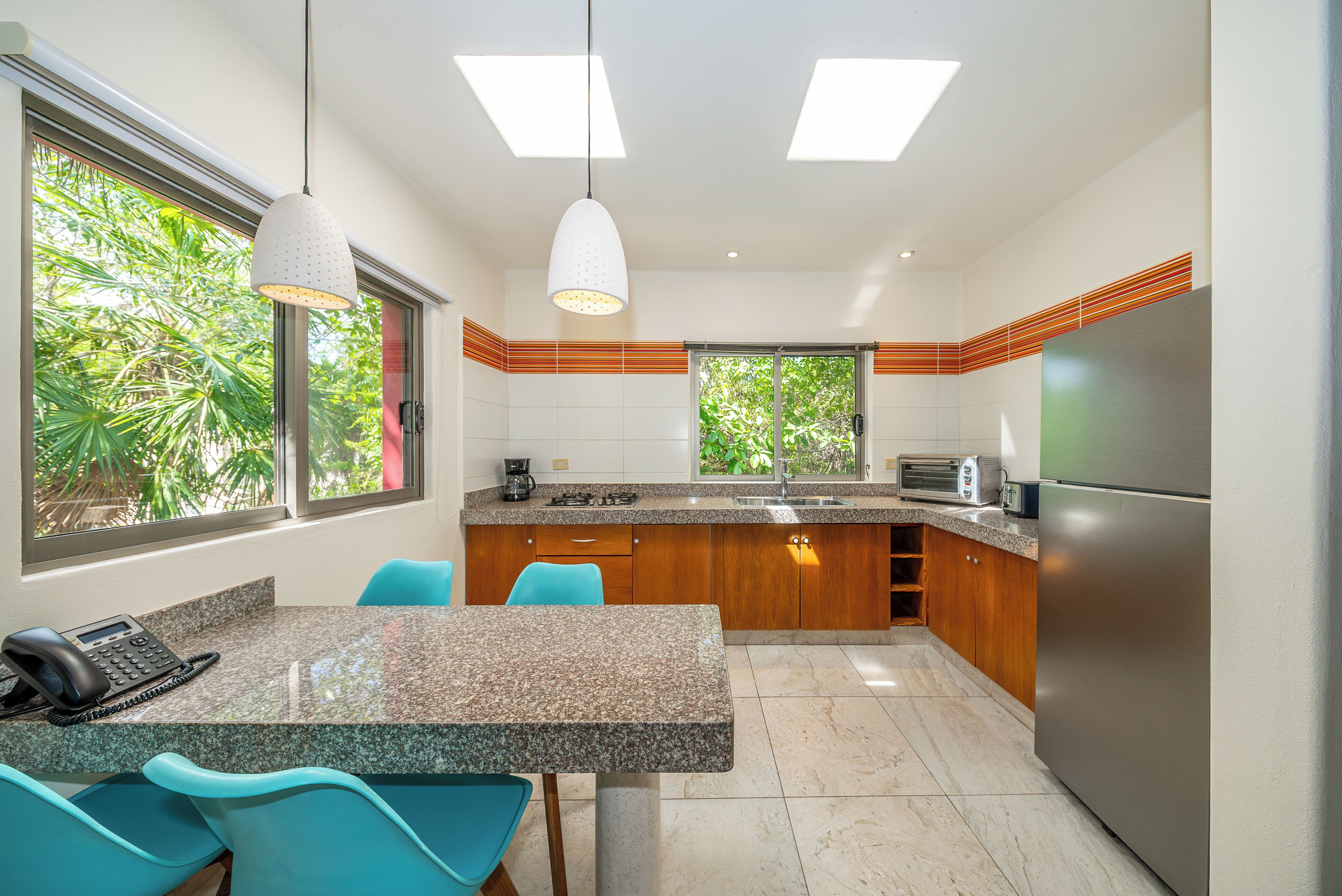 A modern kitchen with granite countertops, a stainless steel refrigerator, and a dining area with blue chairs.