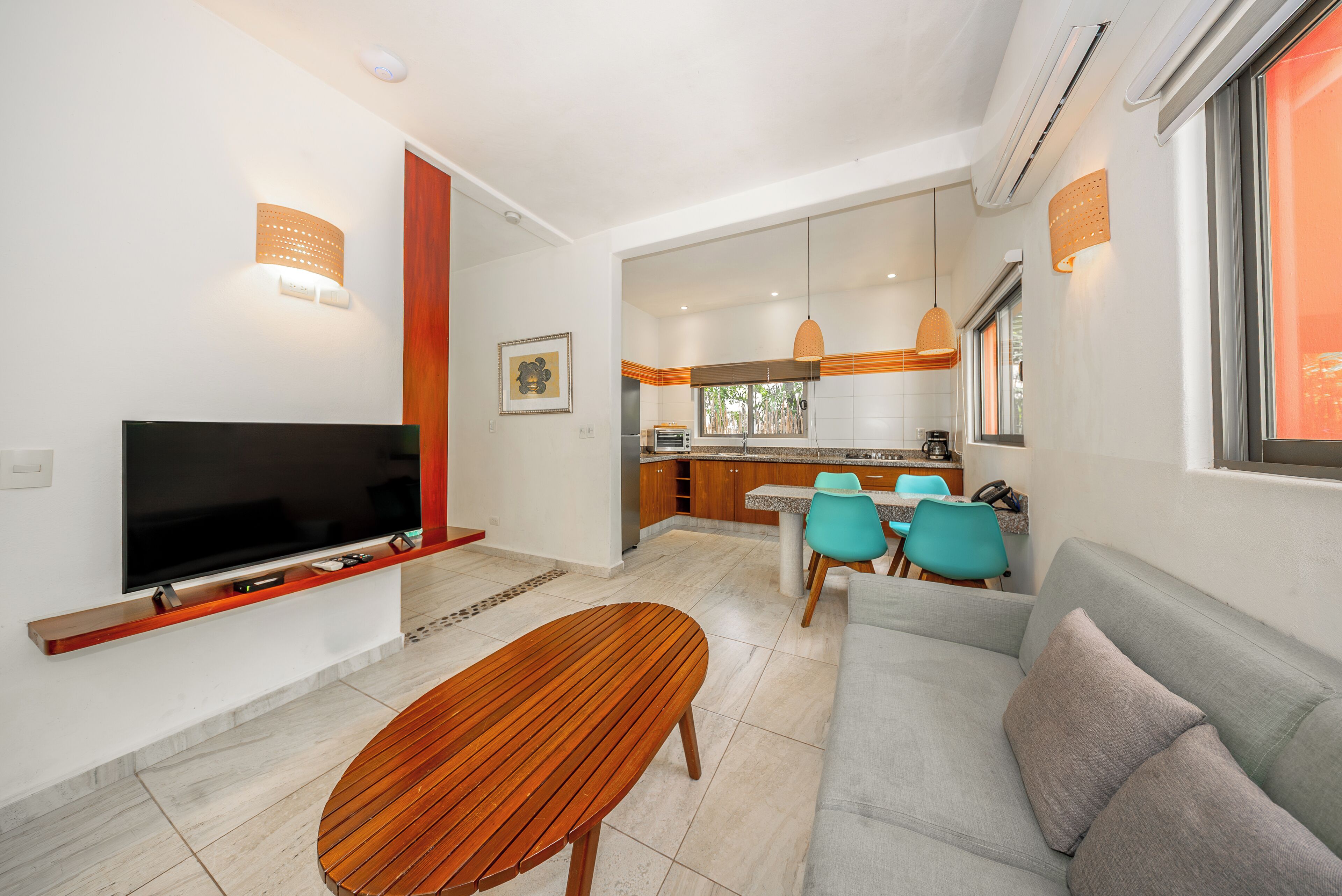 Ein modernes Wohnzimmer mit Flachbildfernseher, Couchtisch aus Holz, grauem Sofa und Türkis-Stühlen.