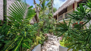 Un camino que lleva a un edificio de techo de paja, rodeado de exuberante vegetación tropical.