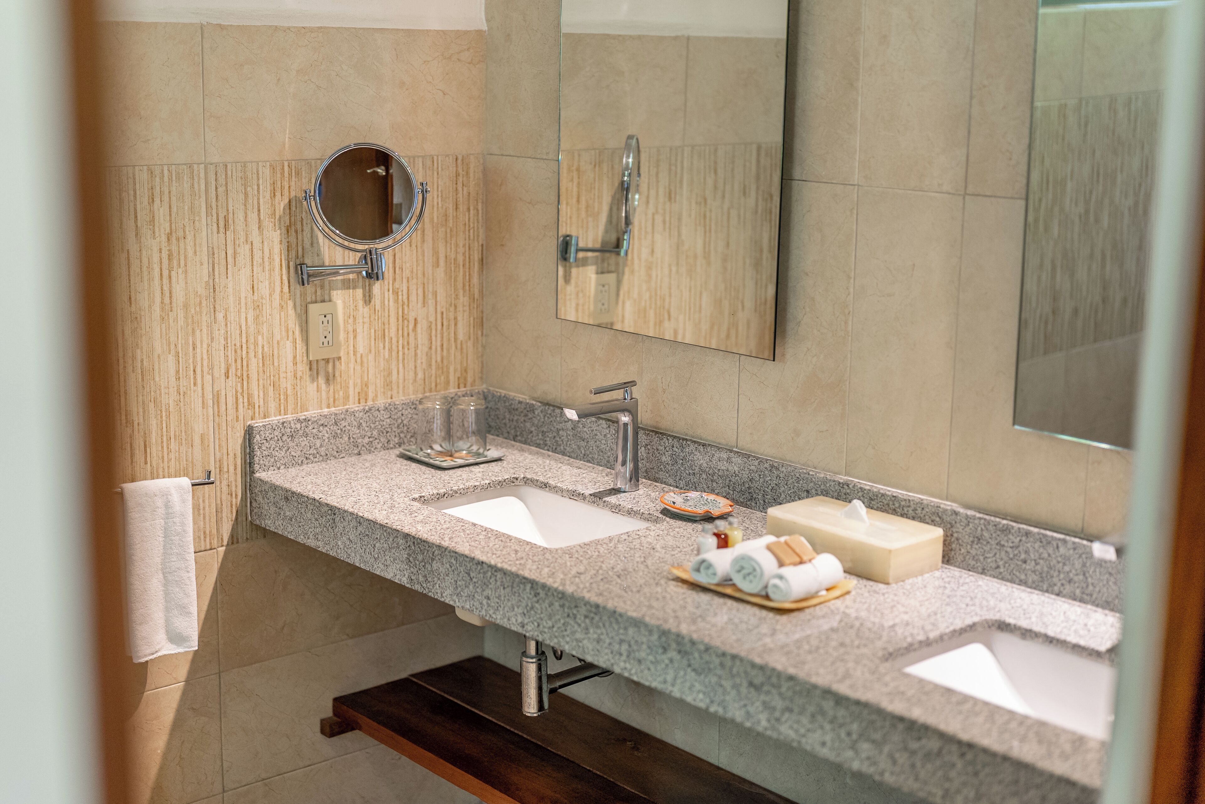 A bathroom with a granite countertop, two sinks, a mirror, and a towel rack.