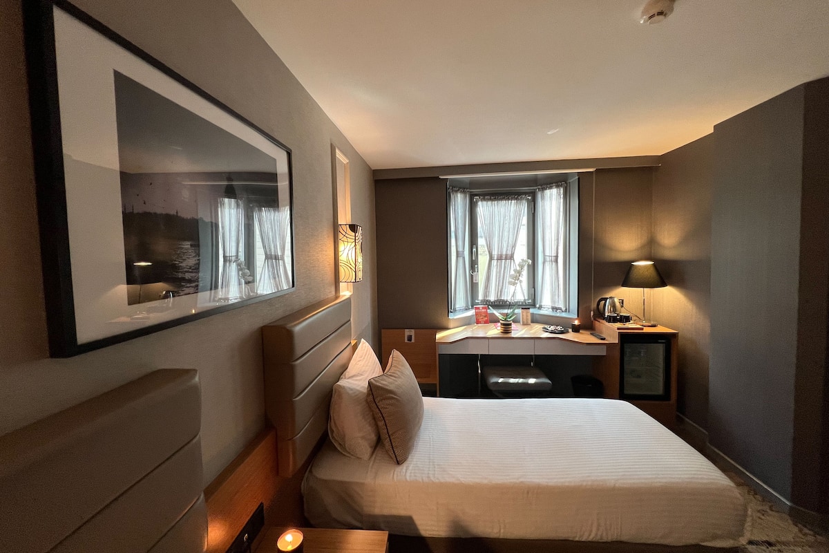 Habitación de hotel con cama, mesita de noche, lámpara y un espejo grande.
