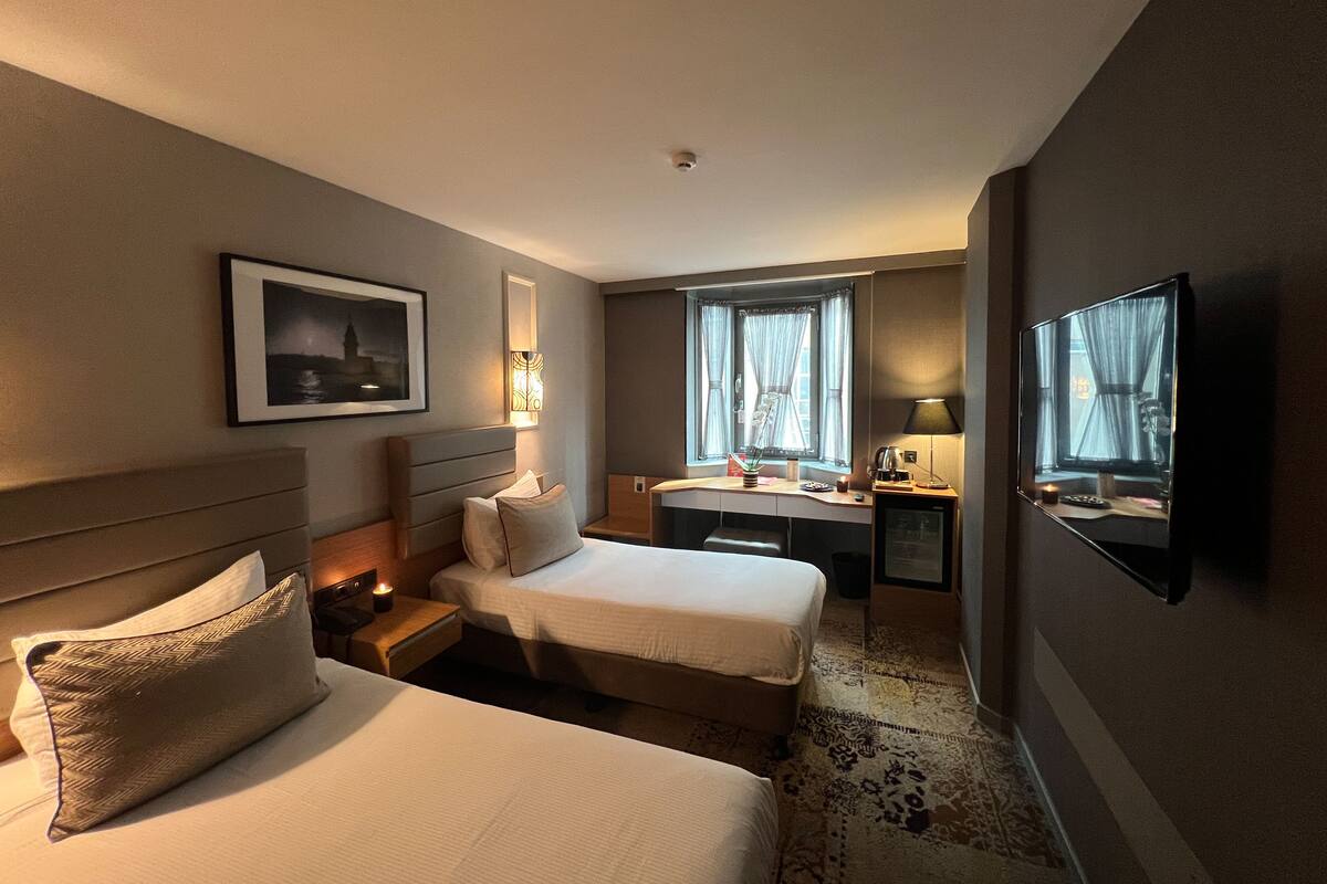 Habitación de hotel con dos camas, un escritorio, una silla, un televisor y una ventana con cortinas.